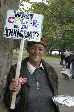 Stan Schnier, A woman at the Immigrant Workers Freedom Ride holds a sign that asks “What color is an immigrant?”, Flushing Meadows Corona Park, New York, New York, October 4, 2003.  