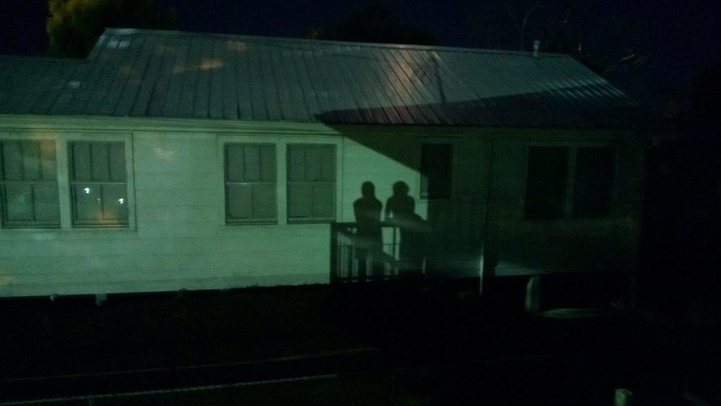 The shadows of two people against a gray-green building, likely at nighttime.