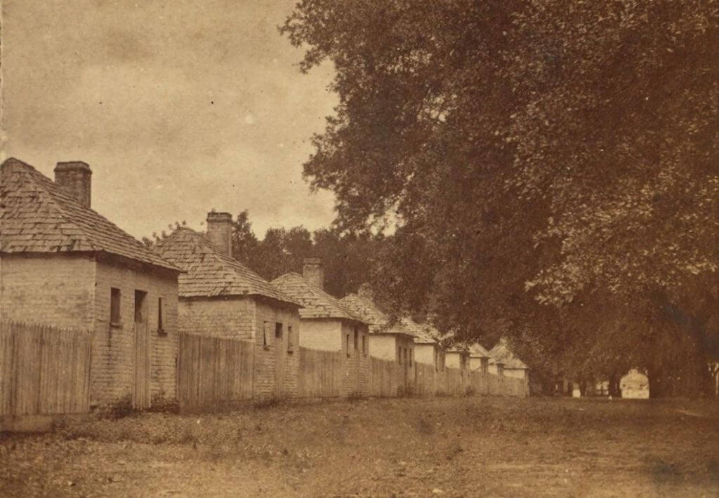Sepia photograph of former slave quarters, surrounded by trees.