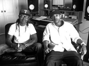 Black and white image of Partners N Crime hip hop group members, wearing casual clothes, sitting in the recording studio.