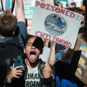 Child holding protest sign that reads "Poisoned Childhood"