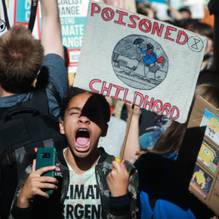 Child holding protest sign that reads "Poisoned Childhood"