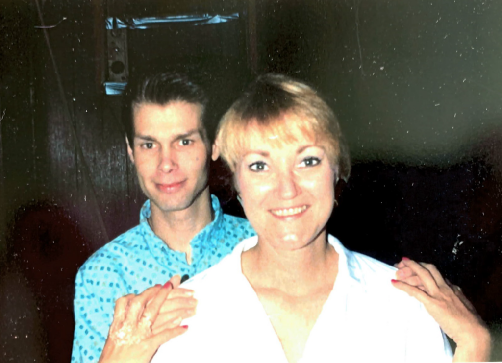 Ruth Corker and Billy Ray Collins smile at the camera. Collins stand behind Burks with his hands on her shoulders in a familiar and friendly manner.