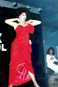 Billy Ray Collins performs drag in a long read dress and bright read lipstick.