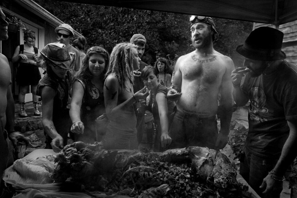 Young people reach for pieces of an outdoor roasting hog.