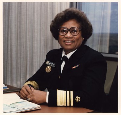 A formal portrait of Dr. Joycelyn Elders, a Black woman, sitting at a desk in a military uniform.